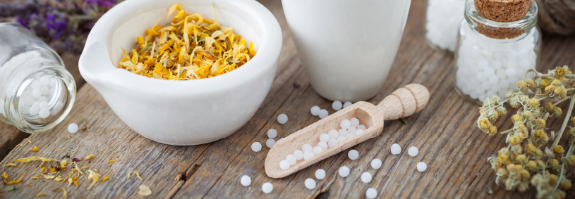 Mortar and bowl of dried healing herbs and bottles of homeopathic globules