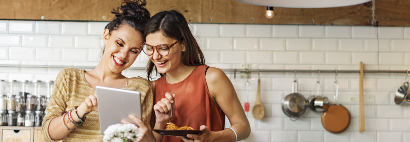 Two women looking at healthy nutritious recipes on iPad together in modern kitchen