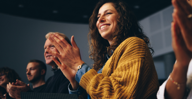 Audience at seminar with lady in a yellow jumper clapping as the primary image focus