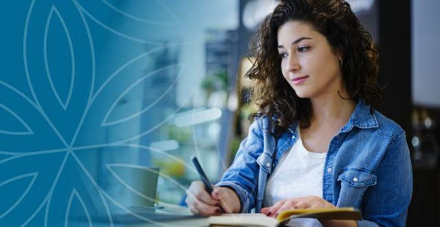 Young woman watching webinar recording on laptop and taking notes