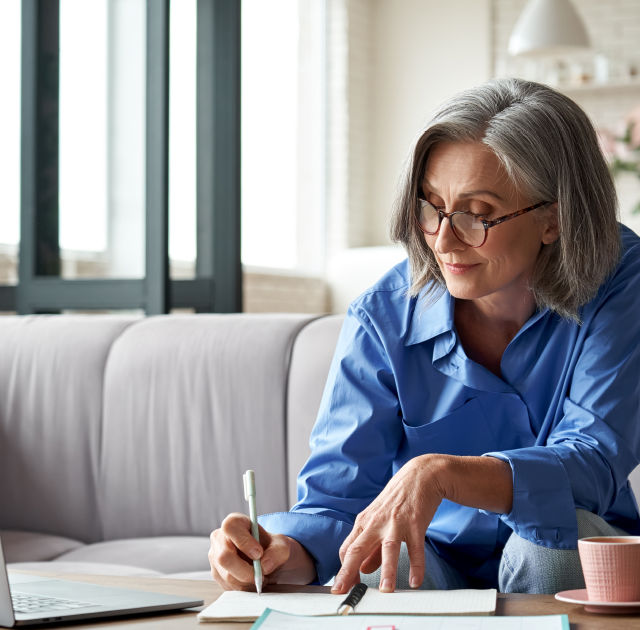 mature women taking notes while watching webinar recording