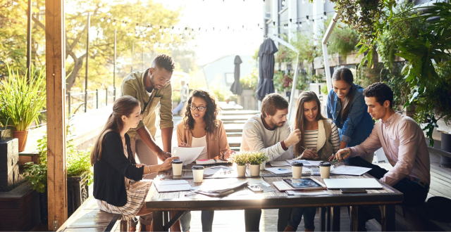 A group of five people seated at a table, reviewing documents and discussing ideas in a collaborative setting.
