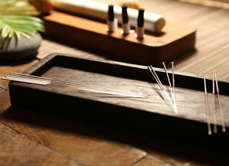Acupuncture needles arranged neatly on a wooden tray, showcasing their slender, metallic design against the natural wood surface.