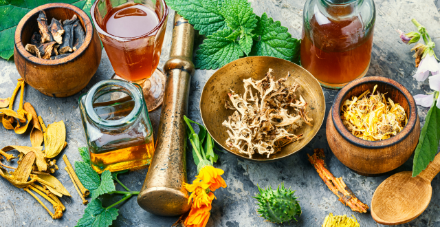 Dried herbs, oils, and botanicals arranged in vintage mortar and pestle, glass jars, and wooden bowls.