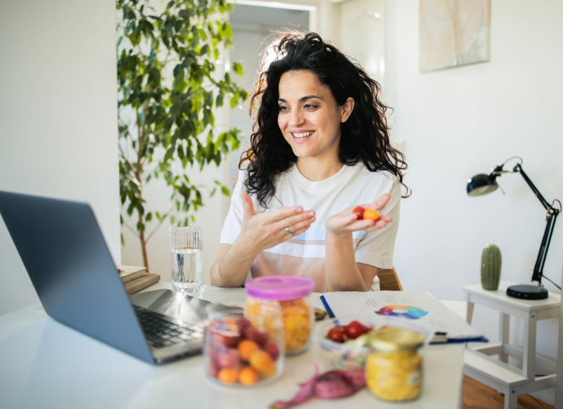 A woman sitting at a table with a laptop, enjoying a meal, focused on her work while surrounded by food.